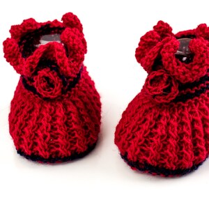 May include: A pair of red knitted baby booties with a blue trim and a crocheted flower detail.