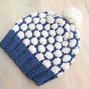 May include: A blue and white knitted beanie with a white pom pom on top. The beanie has a white and blue polka dot pattern.
