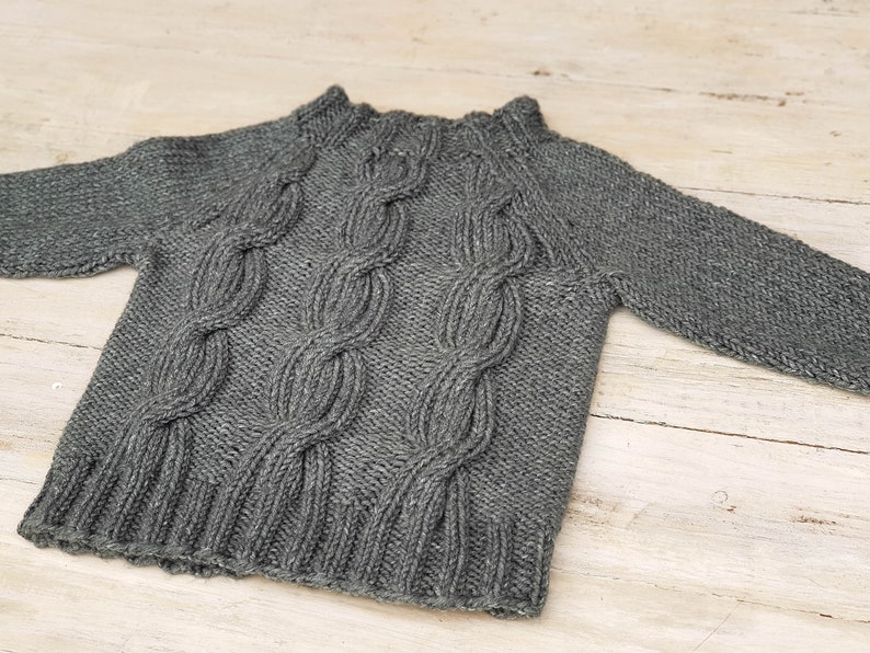 May include: A gray knitted sweater with a cable knit pattern.