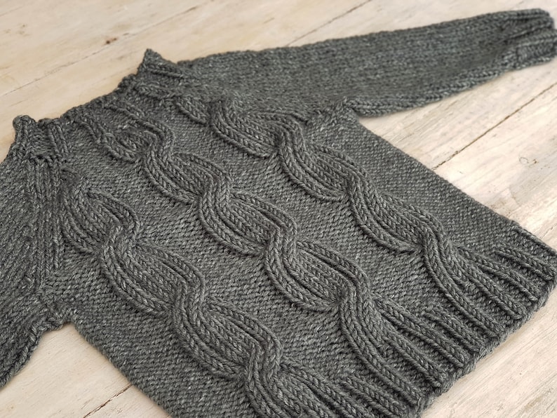 May include: A gray knitted sweater with a cable knit pattern.