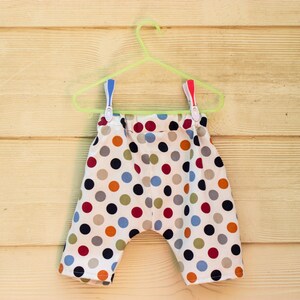 May include: A pair of white cotton shorts with a colorful polka dot pattern. The shorts are hanging on a green plastic hanger.