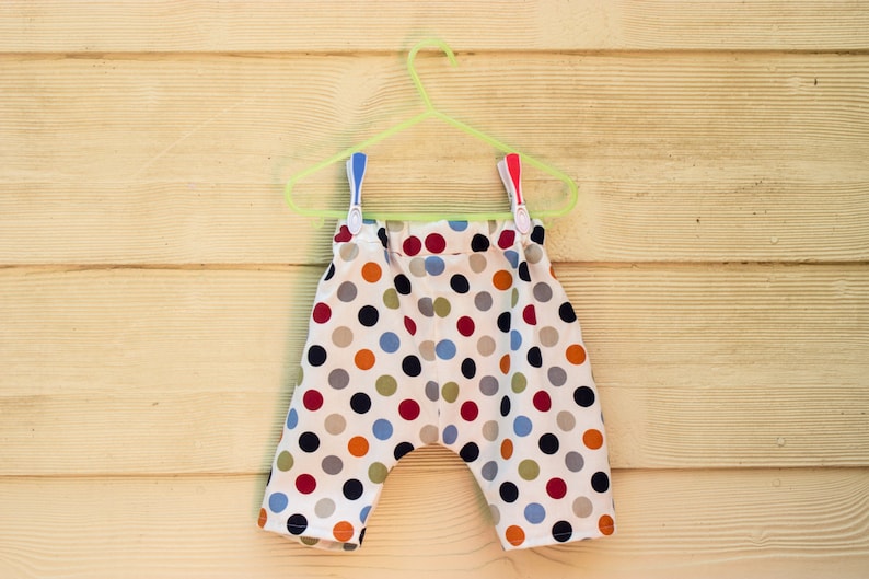 May include: A pair of white cotton shorts with a colorful polka dot pattern. The shorts are hanging on a green plastic hanger.