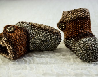 May include: A pair of brown and gray knitted baby booties with a button on each. The booties are made of a soft, textured yarn.
