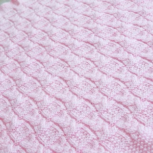May include: A pink knitted baby blanket with a cable knit pattern.