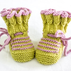May include: A pair of knitted baby booties with green and pink stripes. The booties have a ruffled pink trim and are tied with pink laces.