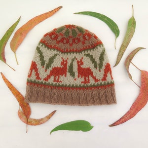 May include: A brown knitted hat with a colorful pattern of orange kangaroos and green leaves. The hat is surrounded by eucalyptus leaves.