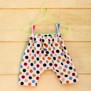 May include: Polka dot patterned pants with a white background and colorful dots. The pants are hanging on a green plastic hanger.