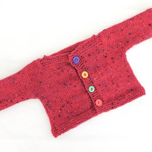 Puede incluir: Un cárdigan de punto rojo para bebé con botones de colores.