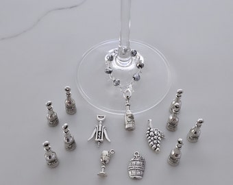May include: A set of silver wine glass charms featuring various wine-themed designs, including wine bottles, grapes, a wine barrel, a corkscrew, and a wine glass. The charms are hanging from a silver chain with clear crystal beads.