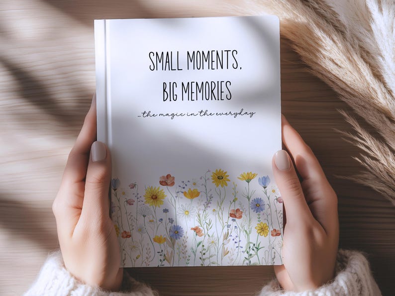 May include: A white notebook with the text "SMALL MOMENTS, BIG MEMORIES" and "the magic in the everyday" printed in black. The bottom of the cover features a colorful illustration of various wildflowers in shades of yellow, blue, and red.