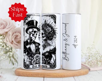 May include: A white cylindrical tumbler featuring a black and white illustration of a skeleton couple in formal wedding attire, including a top hat and floral headpiece. The text reads Till Death, Bethany & Jarrod, and est. 2024 in black script.