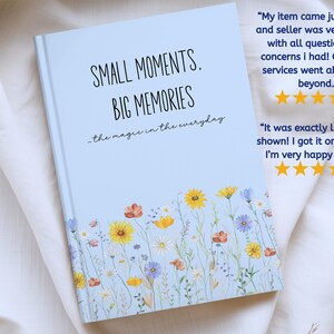 May include: A light blue hardcover journal featuring a floral print at the bottom with yellow, orange, and blue wildflowers. The text on the cover reads: SMALL MOMENTS, BIG MEMORIES, the magic in the everyday. The book has a clean, matte finish.