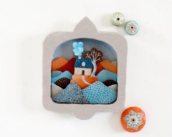 Diorama de pared hecho a mano de una casa en la montaña en azul, gris y naranja
