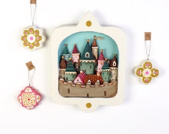 Diorama mural artesanal con castillo de ciudad medieval en tonos tierra cálidos.