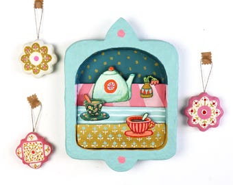 Diorama artesanal con escena de té, estilo acogedor de cabaña para colgar en la pared.