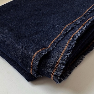 Peut inclure: Tissu bleu marine plié avec une bordure effilochée et des coutures orange. Le tissu semble être un matériau de poids moyen, peut-être du lin ou un textile similaire. Les bords sont effilochés, ajoutant un aspect décontracté et texturé.