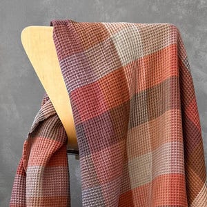 Peut inclure: Une couverture en tissu gaufré à motif écossais dans des tons d'orange, de brun et de beige. La couverture est drapée sur une chaise en bois.