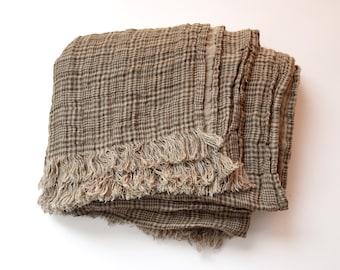 May include: A folded brown and tan plaid throw blanket with fringed edges. The blanket has a textured appearance and is made of a soft, lightweight material. The plaid pattern is a classic design, suitable for a variety of home decor styles.