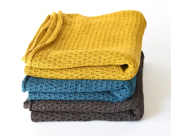 Pode incluir: Uma pilha de três cobertores de malha em amarelo, azul-petróleo e marrom. Os cobertores estão dobrados e empilhados um em cima do outro.