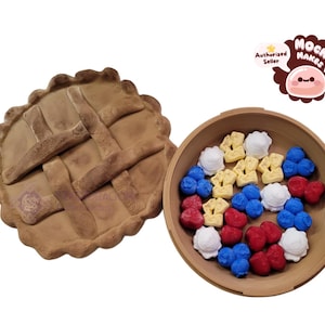 Puede incluir: Una tarta marrón con una corteza de rejilla junto a un cuenco de madera lleno de caramelos coloridos con forma de flor. Los caramelos son rojos, blancos, amarillos y azules. Un logotipo en la esquina superior derecha dice "Mochi Makes."