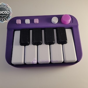 May include: A purple toy keyboard with black and white keys. The keyboard has several buttons and a large pink knob. The top left corner has a VOX3D logo.