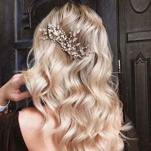 May include: A woman with long, wavy, blonde hair wearing a black top with a low back. She has a silver hair comb with small white beads in her hair.