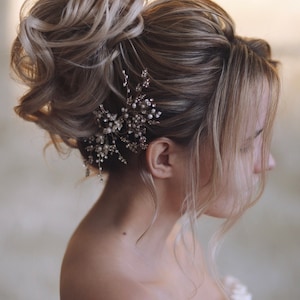 May include: A woman with blonde hair styled in a high bun with a pearl and silver hair comb.
