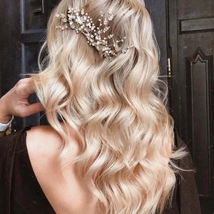 May include: A silver-toned hair comb with crystal and pearl embellishments, set in blonde wavy hair. The comb has a floral design. The hair is styled in loose waves, creating a soft, romantic look.