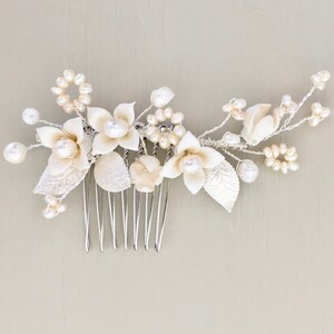 May include: A white floral hair comb with pearl accents. The comb has a silver base and features delicate white flowers and leaves.