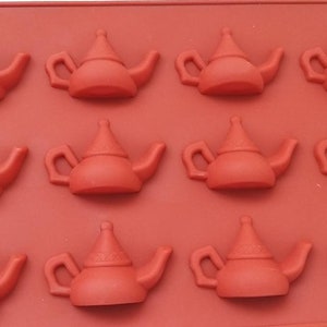 May include: A red silicone mold with 12 cavities shaped like teapots. The mold is designed for making small cakes or other treats.