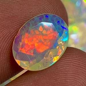 Op de afbeelding: Een regenboogkleurige, ovale opale edelsteen met een facetgeslepen vorm. De opaal vertoont een regenboogkleurige glans, waaronder rood, oranje, geel, groen, blauw en paars.