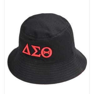 May include: Black bucket hat with red embroidered Greek letters. The hat has a wide brim and a rounded crown. The Greek letters are embroidered in a bold, blocky font. The hat is made of a durable fabric.