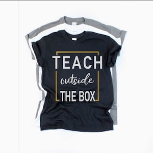 May include: Black t-shirt with the text "TEACH outside THE BOX" in a gold frame.