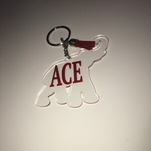 May include: A white acrylic elephant keychain with a red tassel and the word "ACE" in red lettering.