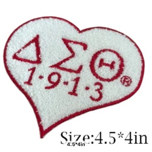 May include: White heart-shaped patch with red embroidered Greek letters, a red circle with a letter H, and the date 1-9-13. The patch is 4.5 inches by 4 inches.