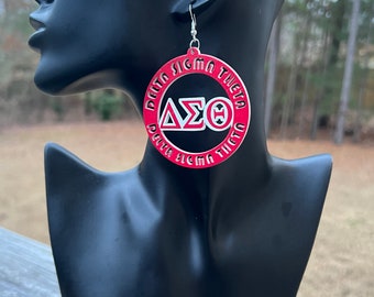 May include: Red and white circular earrings with the text "DELTA SIGMA THETA" and the Greek letters "ΔΣΘ". The earrings are displayed on a black mannequin head. The earrings have a silver hook.