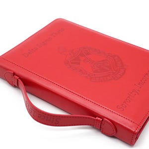 May include: Red leather binder with a handle and the text "Delta Sigma Theta Sorority, Incorporated Since 1913" embossed on the front. The binder features a crest with the Greek letters "Delta Sigma Theta" and a torch.