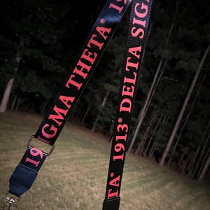 May include: Two black straps with red text. One strap says "1913 DELTA SIGMA" and the other says "1919 SIGMA THETA".