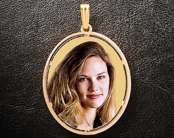 May include: A gold oval pendant with a photo of a woman with long blonde hair. The pendant has a simple design with a smooth surface.
