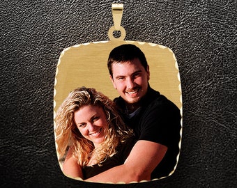 May include: Gold pendant with a photo of a couple. The pendant is square shaped with a scalloped edge. The photo shows a man and a woman smiling.