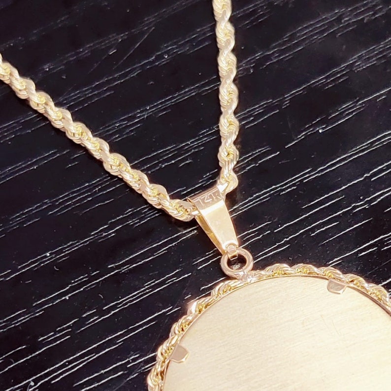 May include: A gold rope chain necklace with a round pendant. The pendant has a smooth, polished surface and is attached to the chain with a small, gold loop. The back of the pendant has the inscription "14K" engraved on it.