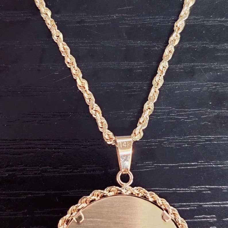 May include: A gold rope chain necklace with a round pendant. The pendant has a smooth, polished surface and is marked "14K" on the back.