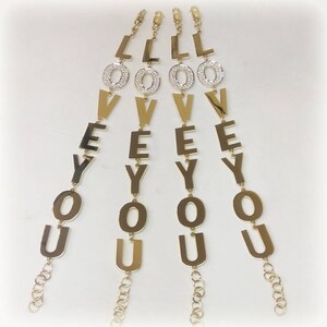 Puede incluir: Cuatro pulseras de oro con la palabra "LOVE YOU" escrita en letras grandes. Cada letra est&aacute; adornada con peque&ntilde;os diamantes de imitaci&oacute;n transparentes.