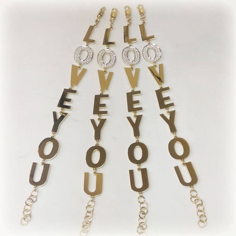 Puede incluir: Cuatro pulseras de oro con la palabra "LOVE YOU" escrita en letras grandes. Cada letra est&aacute; adornada con peque&ntilde;os diamantes de imitaci&oacute;n transparentes.