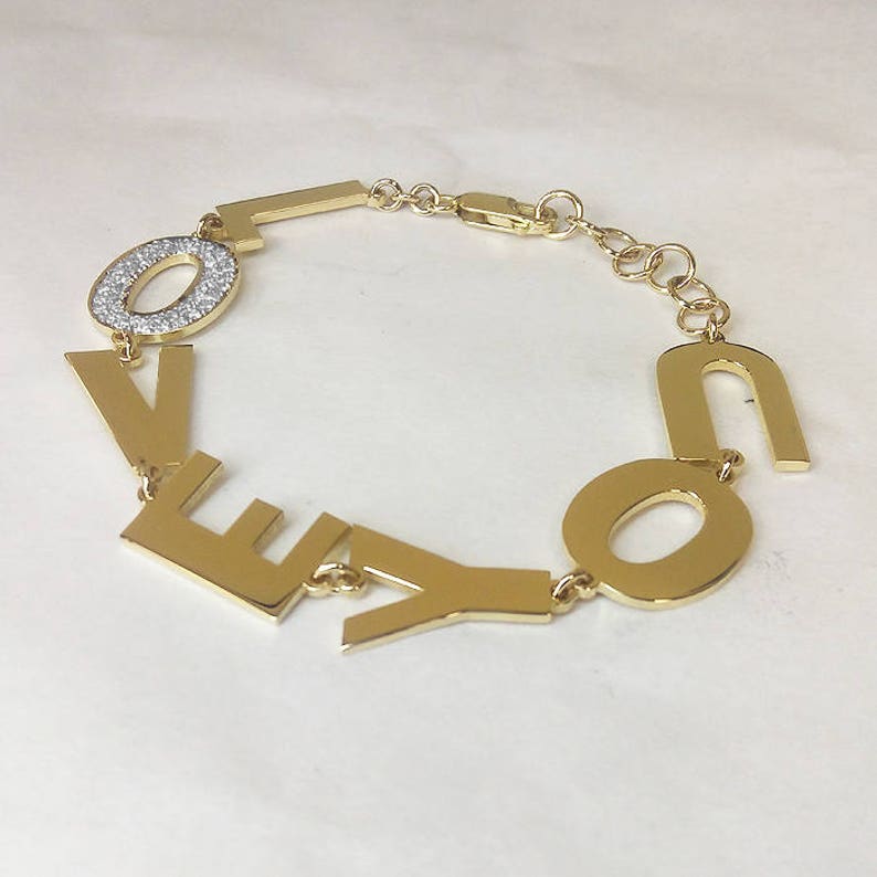 Puede incluir: Pulsera de oro con la palabra "LOVE" escrita en letras individuales. La "O" est&aacute; adornada con peque&ntilde;as piedras transparentes.