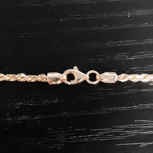 May include: A gold rope chain necklace with a lobster clasp. The clasp is engraved with the words "EDWIL" and "VIENCE".