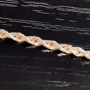 May include: A close-up of a gold rope chain necklace. The chain is made of small, round links that are twisted together to create a rope-like effect.