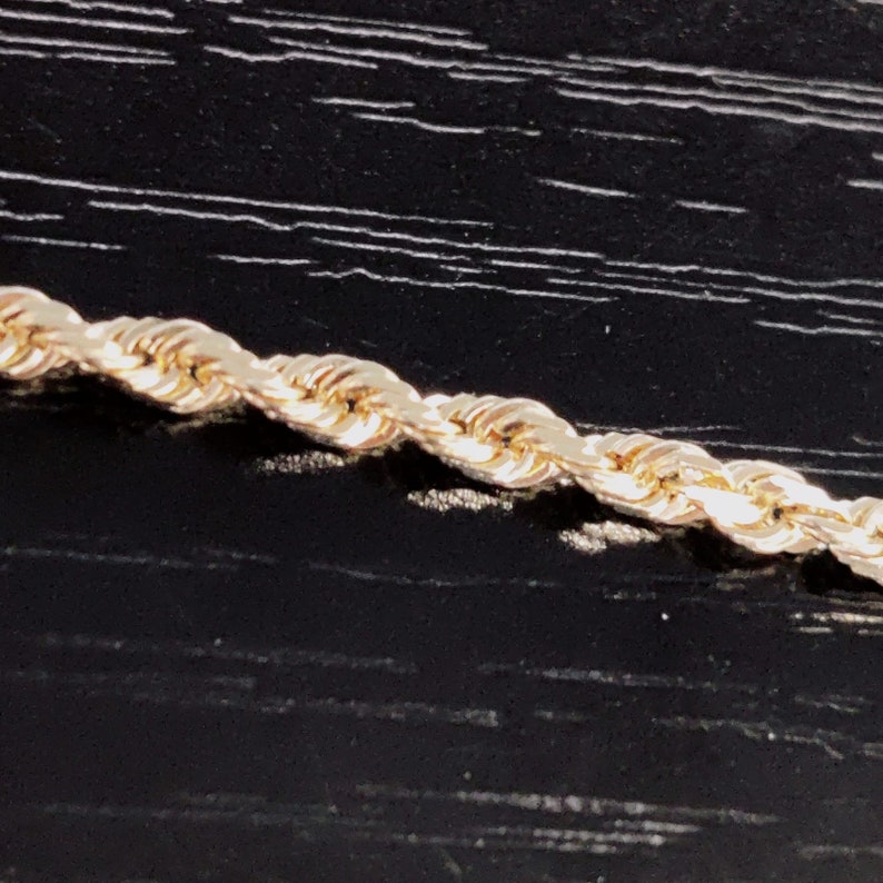 May include: A close-up of a gold rope chain necklace. The chain is made of small, round links that are twisted together to create a rope-like effect.