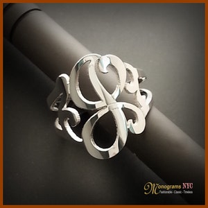 May include: A silver ring with a monogram design. The ring is made of a single piece of metal and has a delicate, intricate design.