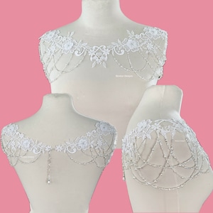 May include: White lace bridal shoulder piece with beaded chains and floral accents. The piece is shown on a white mannequin.